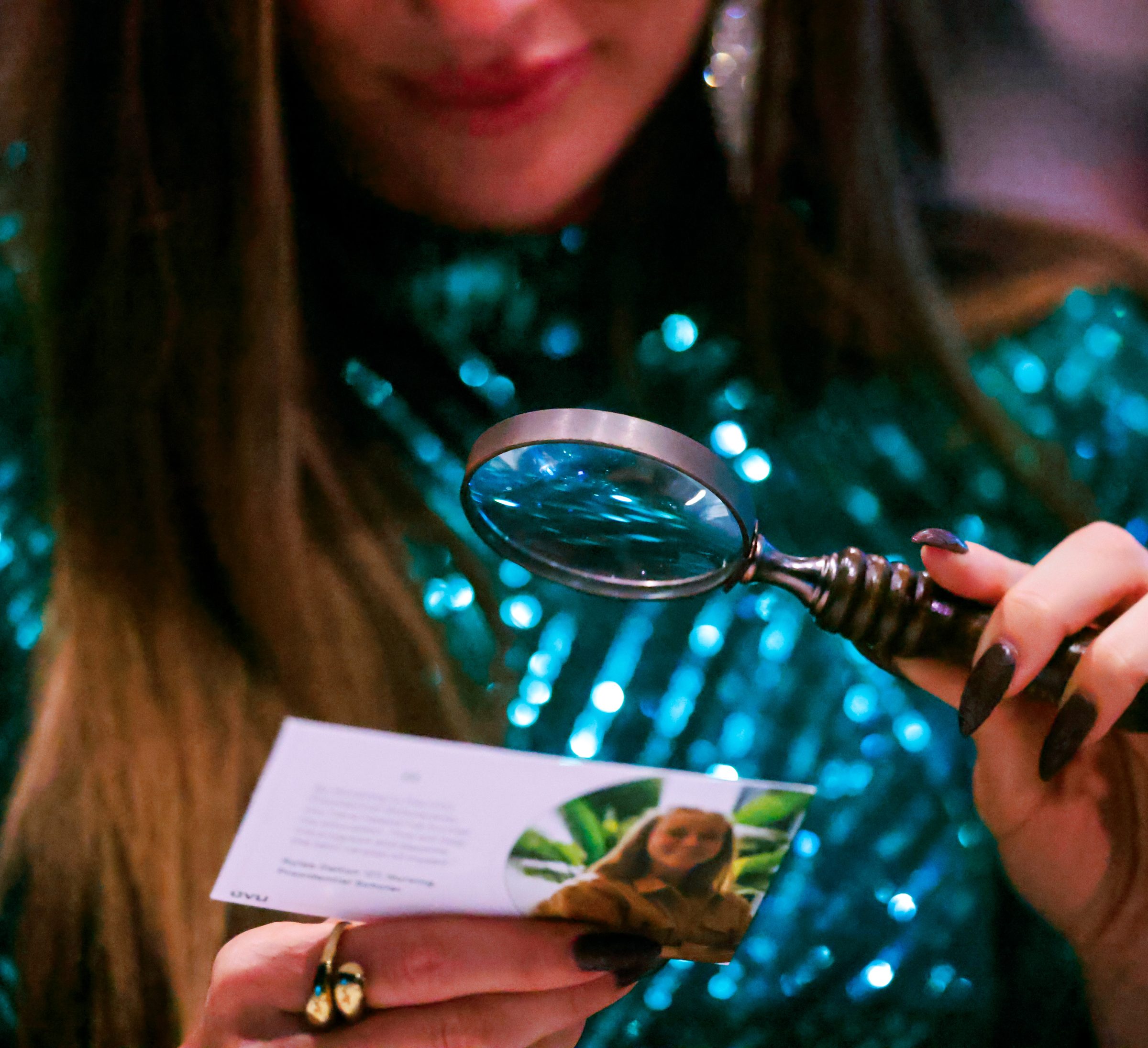 A guest in green sequins reading a PSB 2026 card through a brass magnifying glass